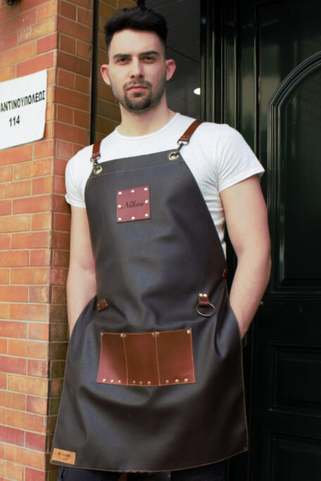 Dark brown leather apron with cross-back straps, light brown pocket, and metal bronze details. Ideal for barbers, stylists, and craftsmen. Customizable leather laser logo options available. Handcrafted for durability and style.