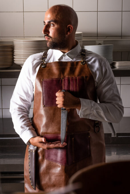 Premium light brown real leather apron with cross-back straps, pockets and handmade knife case. Personalize with your custom logo for a unique touch. Handcrafted for durability and style.