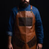 Premium artificial leather apron with pockets, featuring adjustable Italian cow leather cross-back straps and metal bronze details. Ideal for barbers, chefs, and craftsmen. Customizable with laser-engraved logo on chest area.