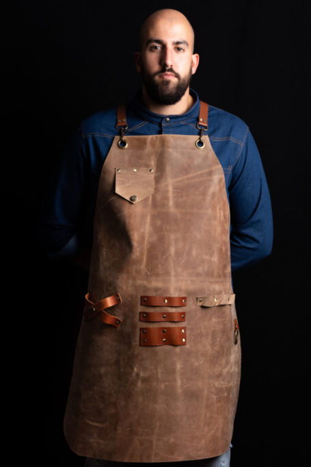 Leather apron in mocha color with cross-back straps, pocket, towel ring, and tool holders. Handmade from 100% genuine Italian leather. Perfect for BBQ, barbers, craft makers, and more. Customizable with your logo. Worldwide shipping available.