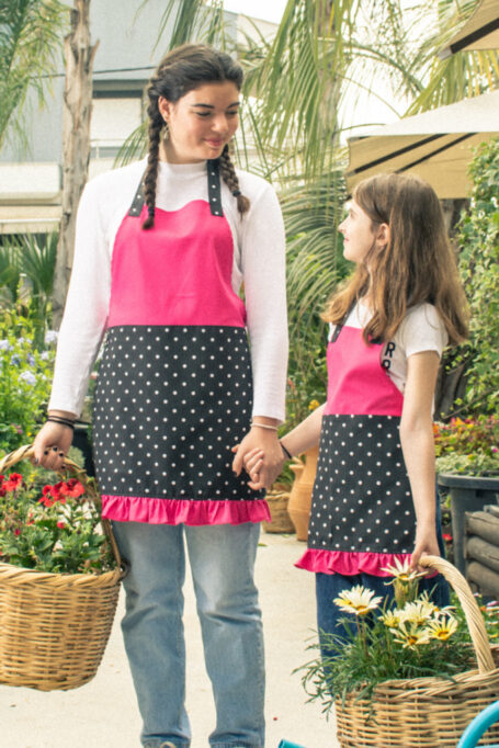 Cute cotton fabric apron in pink color, with black and white polka dot patterned, at neck strap and waist area, designed in sizes for both kids and adults.