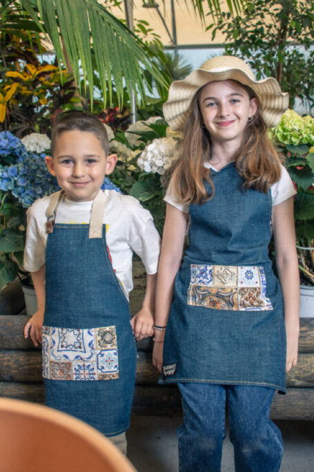 Excellent quality denim kids’ apron in blue color, with adjustable straps and pocket in secondary retro tile pattern fabric for vintage & traditional vibes.
