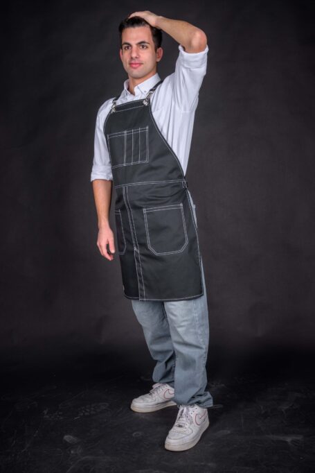 Captivating contrast unfolds as a man wears a white shirt and a custom black apron against a black background. Personalized with beautiful white threadwork on medium-weight cotton fabric.