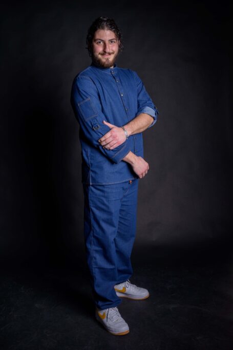 Uniquely designed chef shirt, with external decorative orange thread stitches. Man wearing his beautiful chef jacket with stylish mao collar, metal bronze stud buttons and pockets on sleeves.