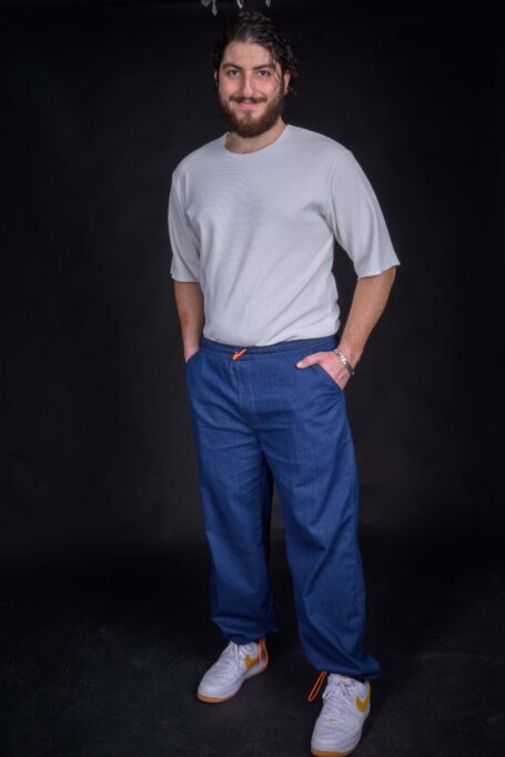 Man wearing his comfortable baggy blue denim pants, which have external decorative orange thread stitches and two front-side pockets.