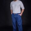 Man wearing his comfortable baggy blue denim pants, which have external decorative orange thread stitches and two front-side pockets.