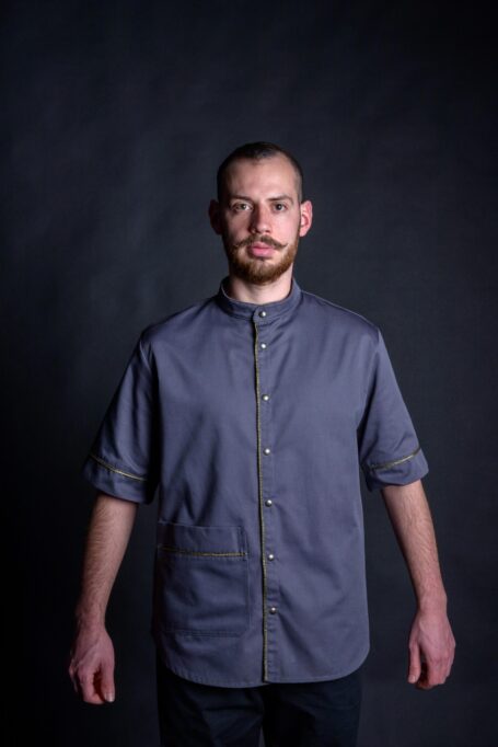 Barber wearing his gray baggy barber smock in black background.