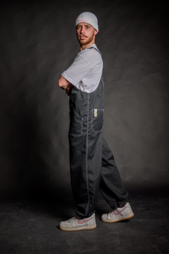 Young man wearing his stylish loose fit overall, made from medium weight durable black fabric.