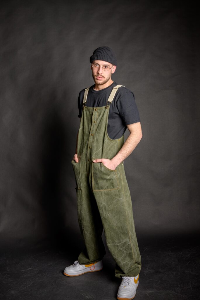 Young man wearing his olive green baggy overall, made from high quality cotton fabric, with metal bronze stud buttons and two front pockets.